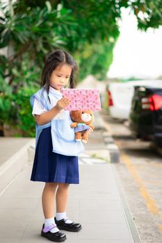 Little asian girl in Thai school uniform holding gift box and doll in the school