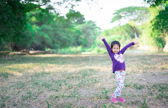 Happy little girl standing with raised hands on the field in the morning