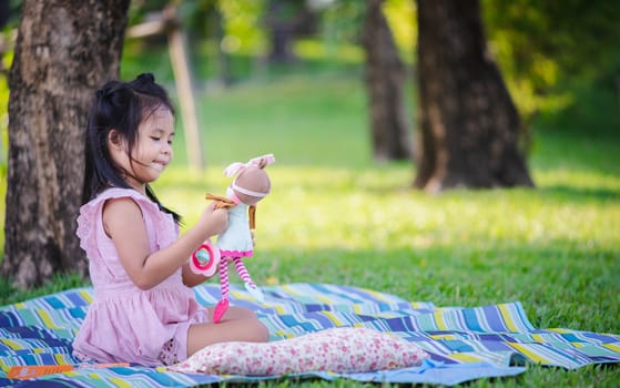 Cute little asian girl sitting with a doll in the park