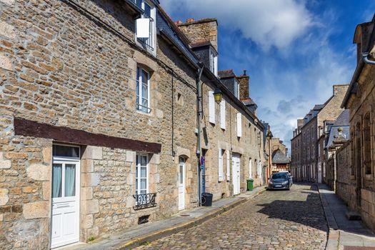 Beautiful view of scenic narrow alley with historic traditional houses and cobbled street in an old town of Dinan with blue sky and clouds. Brittany (Bretagne), France