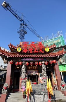 KAOHSIUNG, TAIWAN -- MAY 15, 2015: Old and New -- New building construction towers over the traditional Tsi Tian Temple in Kaohsiung City.