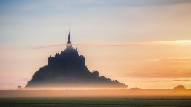 Panoramic view of famous Le Mont Saint-Michel tidal island in beautiful sunrise foggy light, Normandy, northern France