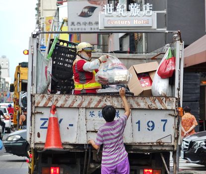 KAOHSIUNG, TAIWAN -- AUGUST 7, 2017: A woman passes a bag to a worker on a truck that collects recyclable materials.
