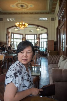 Asian women 40s white skin in white and black dress have a lovely turn face gesture wait for something in a coffee shop cafe vintage style