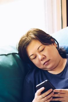 Asian women 40s white skin and plump body in blue dress holding smartphone have a doubt and think gesture on a blue sofa near window