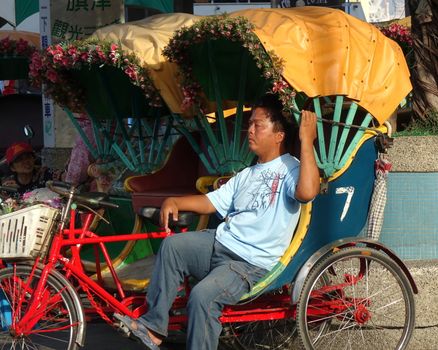 KAOHSIUNG, TAIWAN -- DECEMBER 22, 2018: A driver for a traditional cycle rickshaw rests in the afternoon sun while waiting for passengers.
