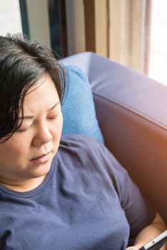 Asian women 40s white skin and plump body in blue dress holding smartphone have a doubt and think gesture on a blue sofa near window