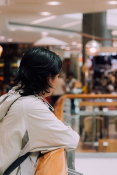 Asian women 40s white skin plump body with backpack and jacket waiting in department store or shopping mall