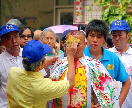 KAOHSIUNG, TAIWAN -- MARCH 16, 2014: At a religious ceremony an unidentified man uses ghost money to wipe the blood from a self-inflicted wound on the forehead of a religious devotee.