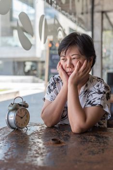 Asian women 40s white skin plump body in black and white shirt have a bored and unhappy gesture between waiting something in a coffee shop cafe with a clock vintage style
