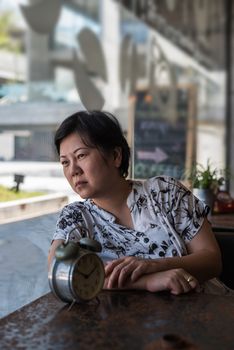 Asian woman 40s white skin plump body in black and white shirt have a bored and unhappy gesture between waiting something in a coffee shop cafe with a clock vintage style