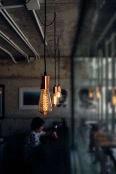Incandescent light bulb with defocus on asia woman 40s white skin in black dress have a doubt and think gesture in a coffee shop cafe