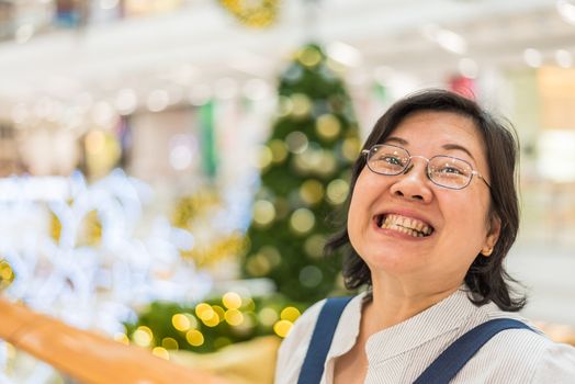 Asian woman 40s white skin plump body with backpack waiting in department store or shopping mall with pine tree in merry christmas and new yaer celebration