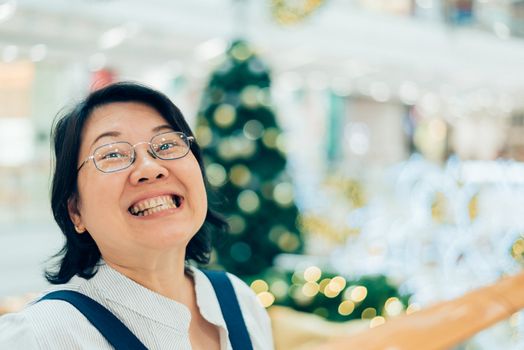 Asian woman 40s white skin plump body with backpack waiting in department store or shopping mall with pine tree in merry christmas and new yaer celebration