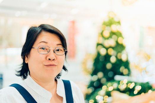 Asian woman 40s white skin plump body with backpack waiting in department store or shopping mall with pine tree in merry christmas and new year celebration