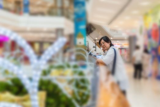 Asian woman 40s white skin plump body with backpack waiting in department store or shopping mall with pine tree in merry christmas and new year celebration