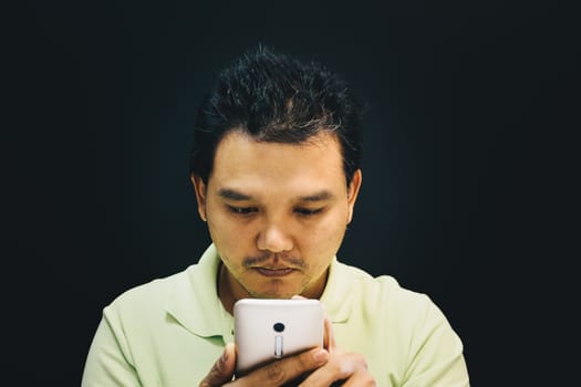 Asian man 40s have a short hair in polo shirt smiling have a thinking gesture with doubt and thoughtful concept using smartphone on black background dark style