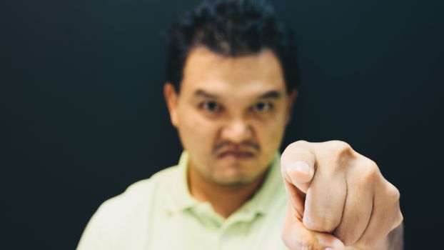 Asian man 40s in green polo shirt do finger pointing at you with anger and crazy gesture in angry or blame concept on black background dark style (Focus on finger)