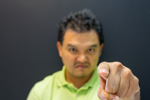 Asian man 40s in green polo shirt do finger pointing at you with anger and crazy gesture in angry or blame concept on black background dark style (Focus on finger)