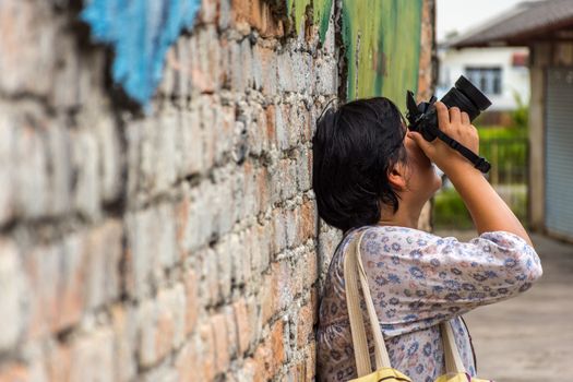 Asia woman plump body holding a DSLR camera standing against a vintage red brick wall when travel