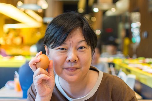 Asia woman plump body holding a egg, defocus blurred on BBQ. yakiniku grill buffet restaurant background. , process in soft orange sun light style