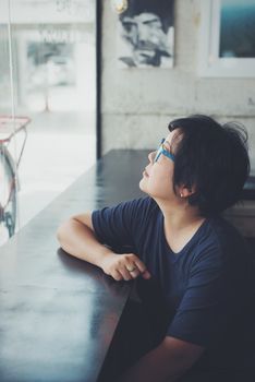 Asian women 40s white skin in black dress with eye glasses have a doubt and think gesture in a coffee shop cafe