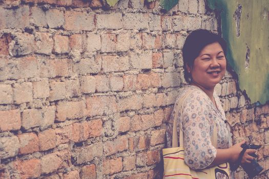 Asia woman plump body holding a DSLR camera standing against a vintage red brick wall when travel , process in vintage style