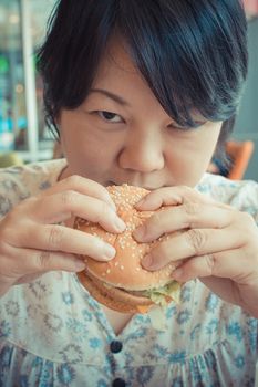 Asia woman plump body eating a hamburger is a unhealthy food at fastfood , process in vintage style