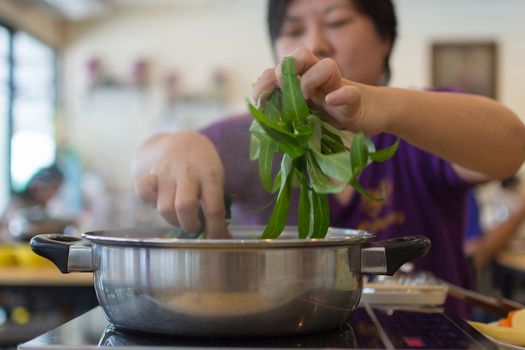 Asia woman plump body cooking food by put a vegetable (morning glory) in to a hot pot for make a sukiyaki or shabu