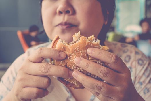 Asia woman plump body eating a hamburger is a unhealthy food at fastfood , process in vintage style