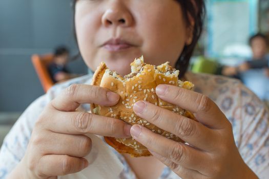 Asia woman plump body eating a hamburger is a unhealthy food at fastfood