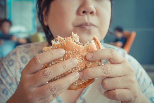 Asia woman plump body eating a hamburger is a unhealthy food at fastfood , process in vintage style