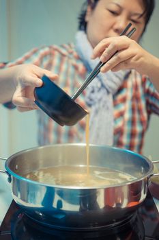 Asia woman plump body cooking food by put a flesh egg in to a hot pot for make a sukiyaki or shabu , process in vintage style