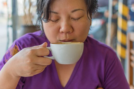 Asia woman plump body drinking a hot coffee in white cup in a cafe