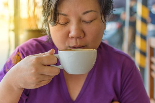 Asia woman plump body drinking a hot coffee in white cup in a cafe , process in soft orange sun light style