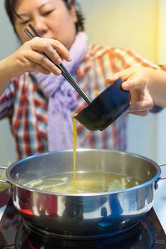 Asia woman plump body cooking food by put a flesh egg in to a hot pot for make a sukiyaki or shabu , process in soft orange sun light style