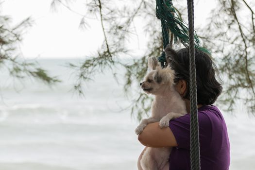 Asia woman plump body and her dog posing on swing at beach with blue sea and sky when travel