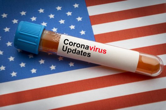 CORONAVIRUS COVID-19 UPDATE text and blood sample vacuum tube on America flags background. Covid-19 or Coronavirus Concept 