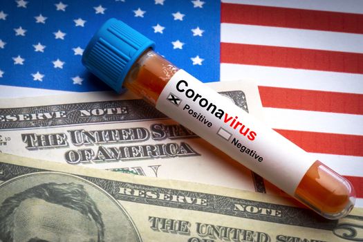 CORONAVIRUS COVID-19 text, US Dollar and blood sample vacuum tube on America flags background. Covid-19 or Coronavirus Concept 