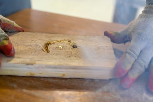 The hands of the master in gloves hold a wooden billet that smokes while working on milling equipment