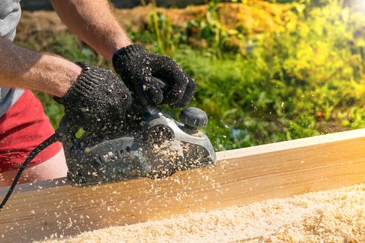 worker, man planing boards with electric tools, chips flying in all directions. Construction, wood processing