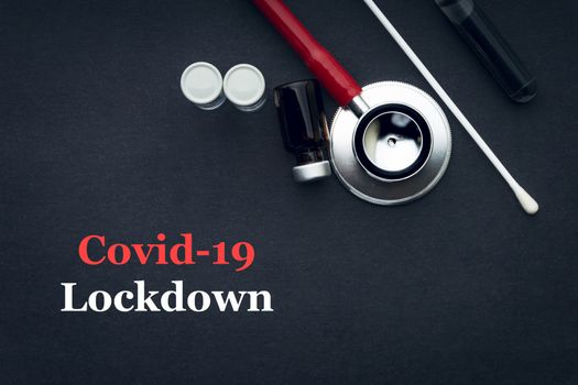 COVID-19 or CORONAVIRUS LOCKDOWN text with stethoscope, medical swab and vial on black background. Covid-19 or Coronavirus concept. 