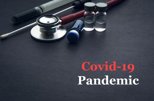 COVID-19 or CORONAVIRUS PANDEMIC text with stethoscope, medical swab and vial on black background. Covid-19 or Coronavirus concept. 