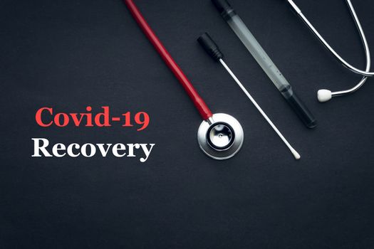 COVID-19 or CORONAVIRUS RECOVERY text with stethoscope and medical swab black background. Covid-19 or Coronavirus concept. 