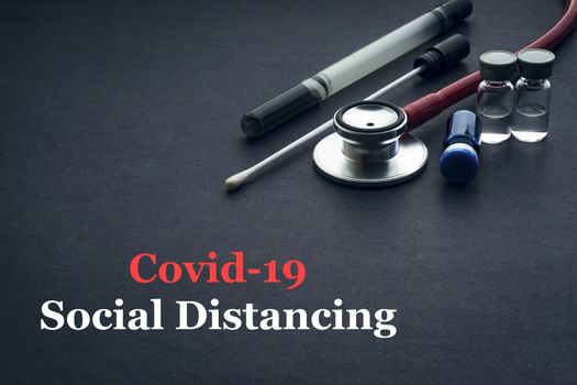 COVID-19 or CORONAVIRUS SOCIAL DISTANCING text with stethoscope, medical swab and vial on black background. Covid-19 or Coronavirus concept. 