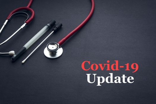 COVID-19 or CORONAVIRUS UPDATE text with stethoscope and medical swab on black background. Covid-19 or Coronavirus concept. 