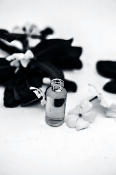 White colored flowers along with leaves and essential organic essence in a small transparent glass bottle isolated on white.