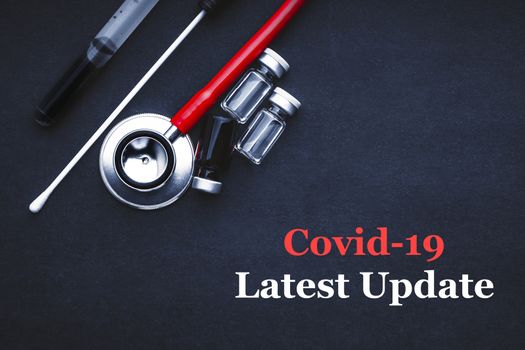 COVID-19 or CORONAVIRUS LATEST UPDATE text with stethoscope, medical swab and vial on black background. Covid-19 or Coronavirus concept. 