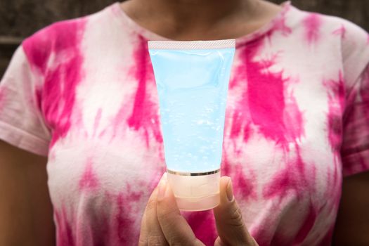 Woman wearing tie-dye clothes, holding one tube of alcohol gel