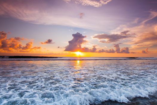 Sea waves at sandy beach at sunset, sun hiding behind a cloud